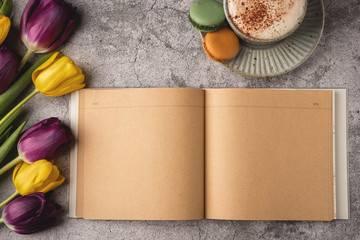 Flat lay, top view of feminine desk. Coffee cup for breakfast, tulips, macaroons, empty notebook. Business planning breakfast concept.