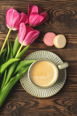 pink tulips, cup with coffee and macaroon cookies on a wooden background, copy space