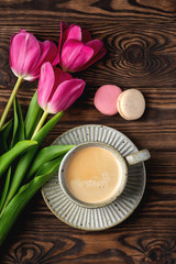Obraz na płótnie Canvas pink tulips, cup with coffee and macaroons on a wooden background, copy space