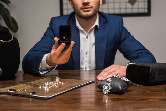 Cropped view of jewelry appraiser holding box with jewelry ring near jewelry and tools on table in workshop