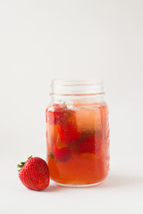 Fototapeta na wymiar Bicchiere con tè rosso, fragole e cubetti di ghiaccio. Sfondo bianco 