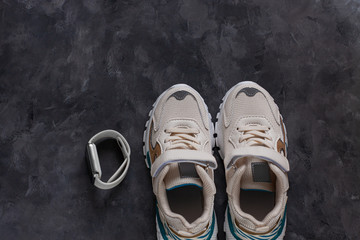 White kids sneakers on a dark grey background flat lay in minimal style. Trendy sports shoes, active lifestyle concept.