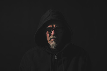 dark portrait of a man with gray beard , hoodie and glasses
