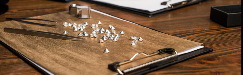 Panoramic shot of tweezers, magnifying glass and gemstones on board on wooden table