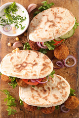 sandwich- pita bread filled with falafel, vegetable and sauce on wooden board