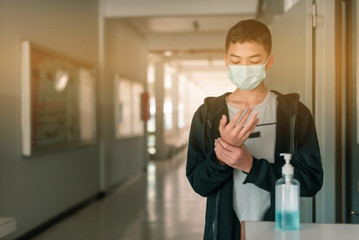A male Asian high school student is wearing the mask and cleaning his hands with alcohol gel before come in the classroom in the midst of Coronavirus disease 2019 (COVID-19) epidemic. - Powered by Adobe