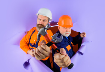 Through paper. Advertising. Worker in helmet. Repairman. Two repairman working with repair tools. Hammer. Spanner. Wrenches. Repair. Builder in construction helmet. Hard hat. Selective focus.