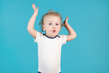 Funny curly girl of two years makes a surprised face and raises her hands up