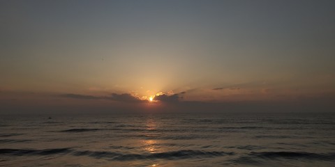 Early morning view of beach with sea waters and sunrise behind
