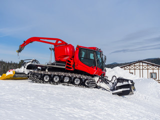 A red snowcat at a ski resort is preparing to tamp the snow. Winter sunny day