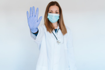 portrait of doctor woman wearing protective mask and gloves indoors. Making a stop sign with hand. Corona virus concept