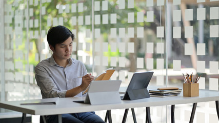 Cropped shot of an Asian male student with a laptop and stationary preparing to complete his thesis to finish university.