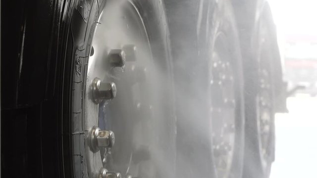 Worker in protective overalls washes truck with water