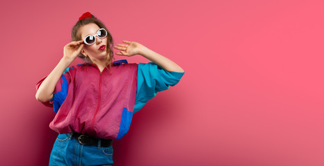 Cool teenager. Fashionable DJ girl in colorful trendy jacket and vintage retro sunglasses enjoys style of 80s � 90s vibes. Teenager Girl at disco party. Young fashion model on coral red background.