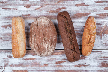 four baguettes of rye and wheat flour of different shapes on a wooden Board in the style of Provence. homemade bread top view