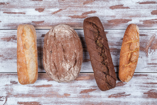 four baguettes of rye and wheat flour of different shapes on a wooden Board in the style of Provence. homemade bread top view - Powered by Adobe