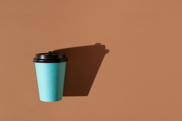 Brown background with one paper blue cup. Trend hard shadow. Copy space.