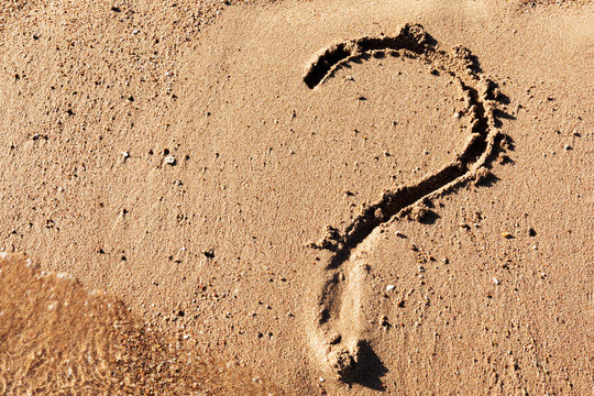Question mark sign on sand beach near the sea. Concept of dilemma, answer and question