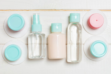 Set of travel size cosmetic bottles on white wooden background. Flat lay of cream jars. Top view of bodycare style concept