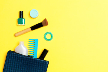 Make up products spilling out of cosmetics bag on yellow background with empty space for your design