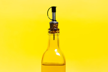 Close-up of glass bottle with olive oil, closed with special cap, isolated on yellow background.