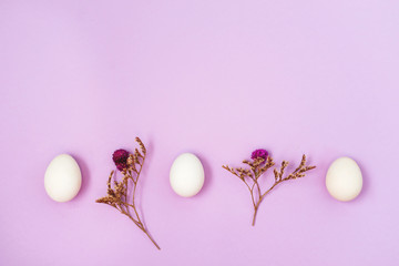 White easter eggs on a lilac background with dry flowers, flat lay, copy text.