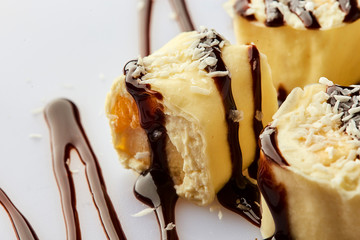 Delicious healthy homemade dessert of bananas, chocolate and cream cheese or ricotta. Banana rolls on a white plate. Treats for kids