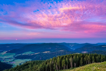Naklejka na ściany i meble Colorful sunset, green mountains and grass, and sky with clouds above the forest