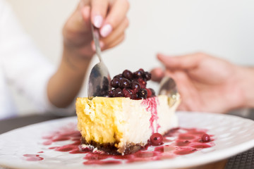 Slice of plain cheesecake with cranberry sauce on white plate. man and woman  eating sweet cake for a perfect dinner - Image