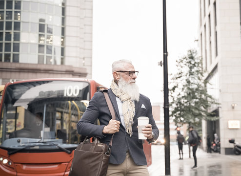 Senior businessman drinking coffee and leaving work. Man walking on a rainy day in the middle of autumn. Man waiting the bus. Work and fashion lifestyle concept - Image