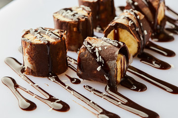 Delicious healthy homemade dessert of bananas, chocolate and cream cheese or ricotta. Banana rolls on a white plate. Treats for kids