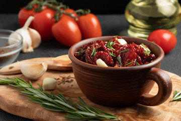 Sun-dried tomatoes with garlic, rosemary and spices in a clay bowl on an olive wood cutting board