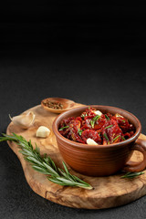 Sun-dried tomatoes with garlic, rosemary and spices in a clay bowl on an olive wood cutting board, vertical image with copyspace