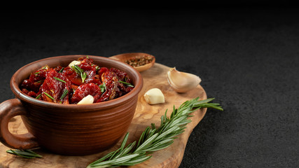 Sun-dried tomatoes with garlic, rosemary and spices in a clay bowl on an olive wood cutting board, copyspace