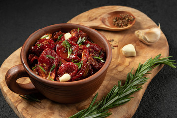 Sun-dried tomatoes with garlic, rosemary and spices in a clay bowl on an olive wood cutting board