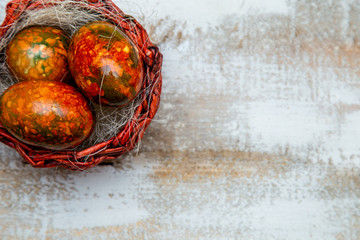 Easter eggs in a red basket lie on a white wooden background.