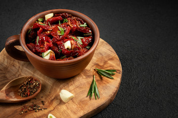 Sun-dried tomatoes with garlic, rosemary and spices in a clay bowl on an olive wood cutting board, copyspace