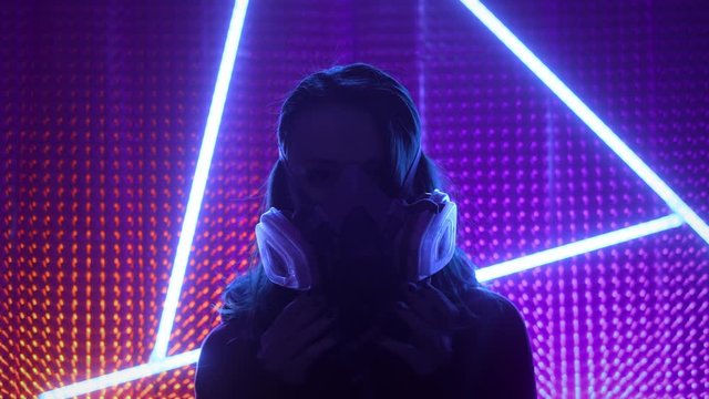 Young girl model in the neon lights of the club. Concept of dubstep or punk style. Wearing a gas mask from dirty air. Protected in a public place from the Chinese coronavirus.