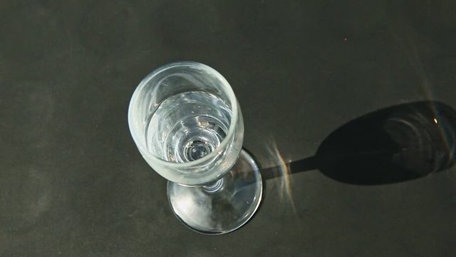 top view on female hand puts single tall crystal wine glass with water on black table