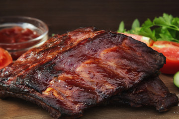 Barbecue pork ribs on a wooden cutting board with ketchup and vegetables