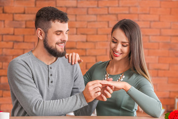 Young man putting ring on finger of his fiancee after marriage proposal at home