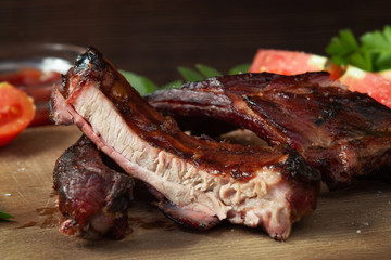 Sliced into pieces barbecue pork ribs on a wooden cutting board with vegetables