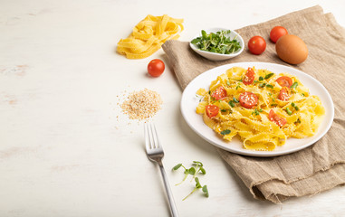 Reginelle semolina pasta with tomato, eggs, sesame and microgreen sprouts on a white wooden background. Side view, copy space.