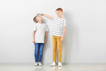 Cute little boys measuring height near light wall