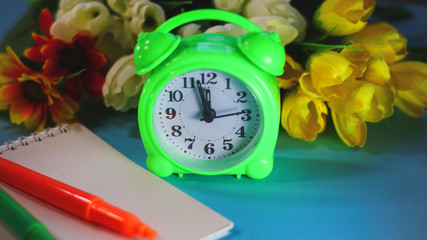 green alarm clock and notebook on a background of flowers.