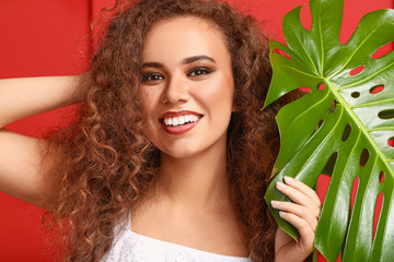Naklejka premium Beautiful African-American woman with tropical leaf on color background