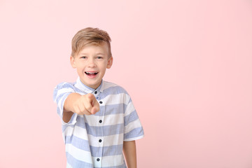 Happy little boy pointing at viewer on color background