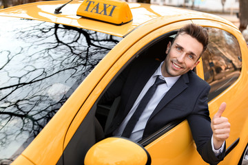 Handsome man showing thumb-up while driving taxi car