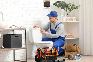 Handsome plumber repairing toilet bowl in bathroom