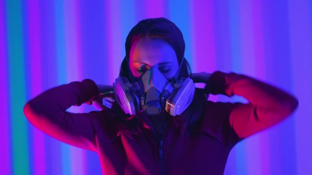 Young girl model in the neon lights of the club. Concept of dubstep or punk style. Wearing a gas mask from dirty air. Protected in a public place from the Chinese coronavirus.